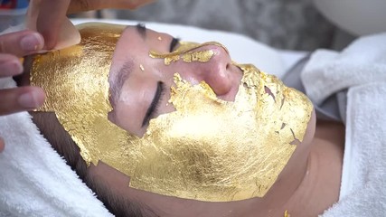 Young woman getting 24 karat gold facial treatment at the beaty clinic. The treatment of using real gold for youthful skin