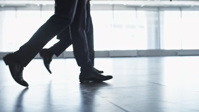 Side view low angled shot of legs of two unrecognizable businessmen walking together through office building lobby