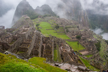Fototapeta premium Classic view of the ancient mysterious city of Machu Picchu with intense clouds on the background in Peru. Astonishing wallpaper image.