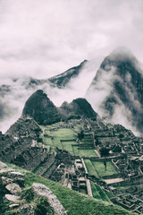 Verical classic view of the ancient mysterious city of Machu Picchu with intense clouds covering the Andes on the background in Peru. Astonishing wallpaper image.