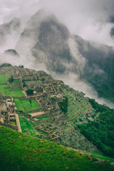 Fototapeta premium The secret and mysterious ruins of Machu Picchu covered in mist with the high Andes mountains on the background. The amazing prize of hiking the Inca Trail in Peru, South America.