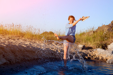 A cheerful dark-haired woman  smiles, walks along the beach, kicks waves, sprays around a lot and enjoys the bright sun on a summer day. Concept of summer holidays at sea and live style