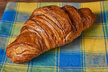Chocolate croissant on a yellow-blue napkin on brown wooden background