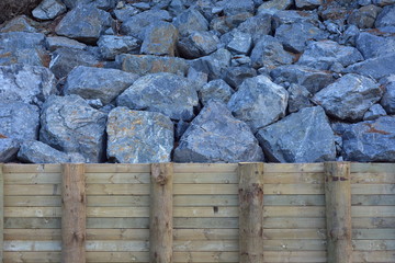Large blocks of blue rock behind wooden retaining wall in steep slope.