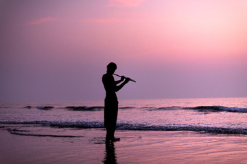 A man is practicing playing the flute on the birch in the sunset. GOA, India. 16.01.2018 - obrazy, fototapety, plakaty