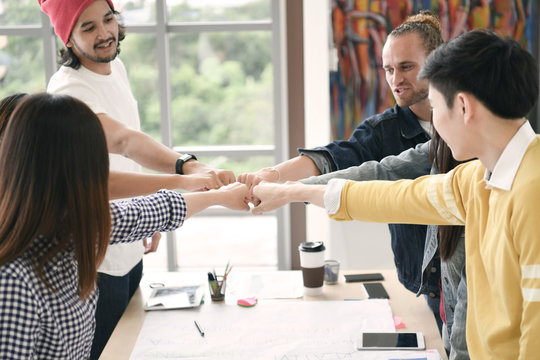 Group of young businesspersons fist-bumping in agreement in a meeting at office