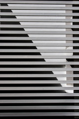 Vertical image of a white metal bar gate whit white wall on the background with a triangular shadow on it. No people.