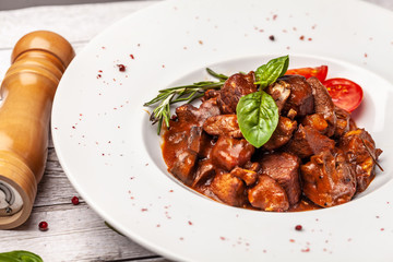 The liver of foie gras and juicy beef meat in a spicy tomato sauce with basil and cherry tamata in a chalk plate on a white, angled table. concept of a beautiful serving of food in a restaurant.