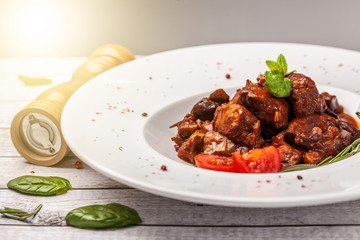 The liver of foie gras and juicy beef meat in a spicy tomato sauce with basil and cherry tamata in a chalk plate on a white, angled table. concept of a beautiful serving of food in a restaurant.