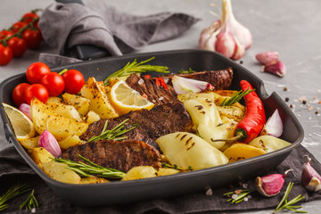 Beef steaks grilled with baked potatoes and vegetables in a pan grill.