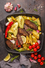 Beef steaks grilled with baked potatoes and vegetables in a pan grill.