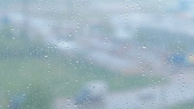 Raindrops flow down the window close-up. View of sity and road from wet window, blur