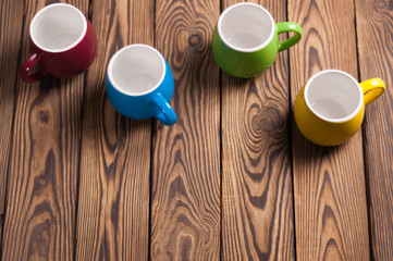 Four colored empty ceramic clean mugs on old worn brown wooden table