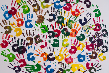 Vertical image of red, yellow, blue, purple, orange and black handprints on a white concrete wall. No people.