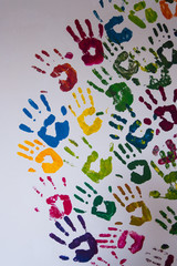 Vertical image of red, blue, yellow, green and purple handprints on a white concrete wall.