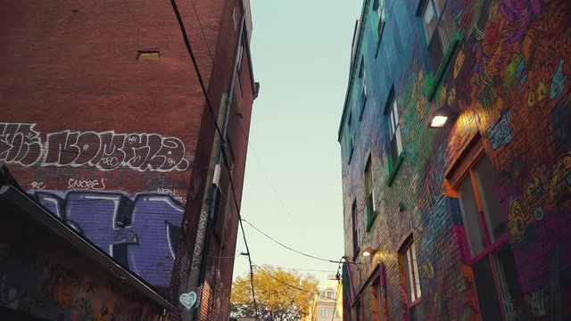 Camera looks up at the graffitied buildings in Graffiti Alley in downtown Toronto