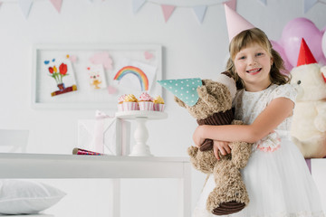 smiling birthday kid holding teddy bear in cone