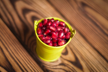 Full metal green bucket of red ripe fresh seeds of pomegranate on old brown weathered rustic planks
