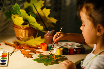 Cute little girl drawing with paint autumn leaves at home
