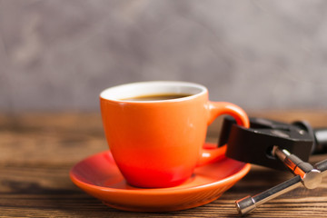 Black metal arm holds orange ceramic mug full of black coffee on old wooden brown table with copy space for your text