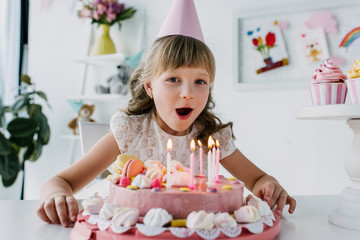 smiling kid in cone blowing out candles from birthday cake