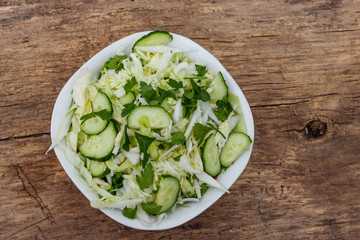 Spring vegan salad with cabbage, cucumber, green onion and parsley on wooden table. Top view