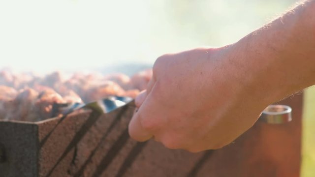 Man cooks shashlik meat on top of charcoal grill on backyard. Close-up hand.