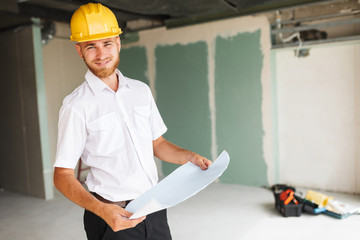 Smiling architect in white shirt and hardhat joyfully looking on plan of new apartment at work