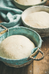 Sourdough for baking homemade wheat flour bread in baskets over rustic wooden kitchen table background, selective focus, close-up