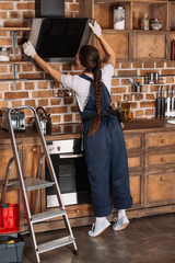 Fototapeta na wymiar young repairwoman in overall examining stove hood at kitchen