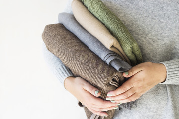 A stack of plaids and scarves in the hands of a woman in a gray sweater. Preparation in cold autumn...