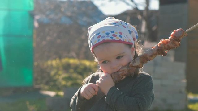 Little cute girl eats barbecue shashlik on a skewer.