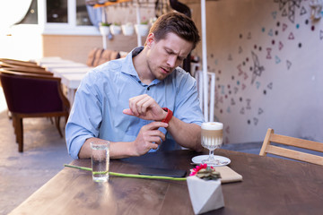 Wrist watch. Handsome good-looking stylish man looking at his nice red wrist watch while running...