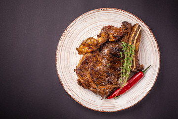 A large piece of juicy pork steak with sauce, with red pepper, on a plate of ceramics on a black background. side view, copy space, top view