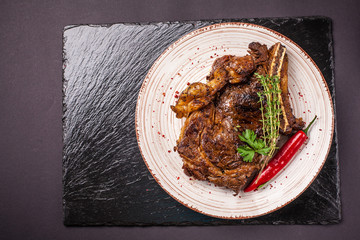 A large piece of juicy pork steak with sauce, with red pepper, on a plate of ceramics on a black background. side view, copy space, top view