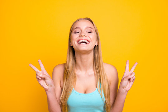 So happy! Young and adorable blond girl happily laughs and demonstrating two fingers v-sign isolated on yellow background