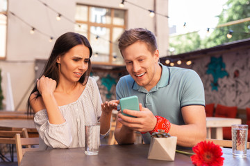 Curious news. Modern good-looking woman and man reading curious news while holding smart phone in hands