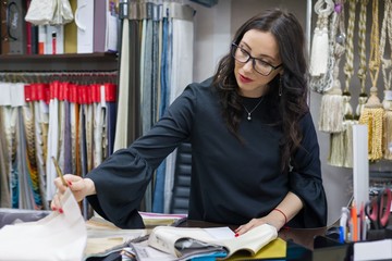 Woman owns a store of interior fabrics and decor works with samples of materials. Small business home textile shop.