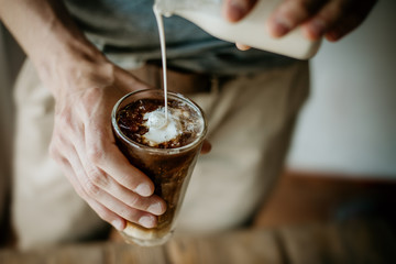 Man pouring milk in iced coffee