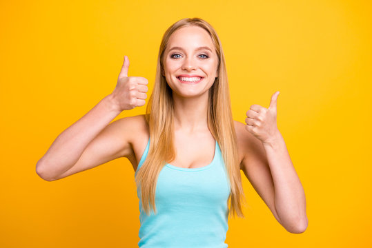 Portrait of young blond woman isolated on yellow background. Female model with toothy beaming smile giving thumbs up success hand sign