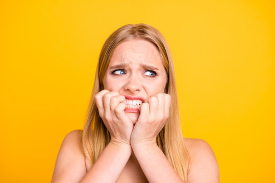 Woman with nervous expressions face, keeps hands near mouth and stare with big eyes against yellow background. Studio shot of frightened young woman, people and fear concept