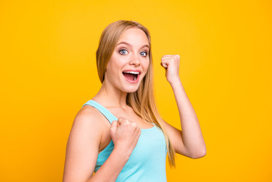 Dynamic image of happy woman celebrating being of victory clasps her hands into fist and make big smile. Close up of female model stands half a turn and isolated on yellow background with copyspace