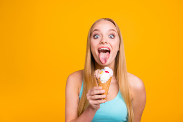 Close up of beautiful blond girl holds an ice cream cone in her hands and pops out a tongue to...