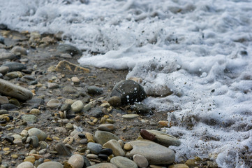 pebble stones on the sea beach, the rolling waves of the sea with foam