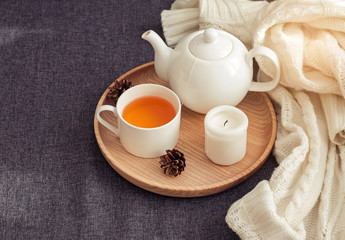 Teapot, cup and candle on the wooden tray standing on the sofa