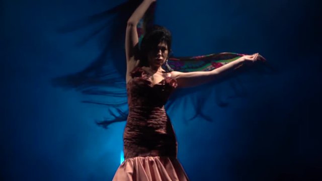 Woman is dancing with a manton in her hands . Light from behind. Smoke blue background. Slow motion