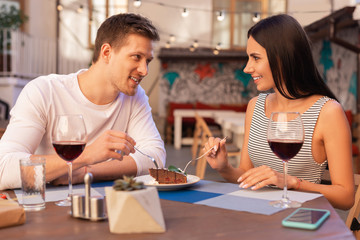 Sweet dessert. Smiling beaming woman eating sweet dessert with her loving man while sitting in the restaurant