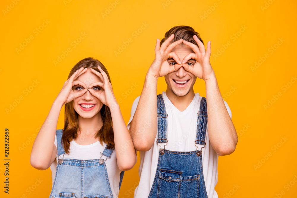 Sticker Close up portrait of playful adorable young cute couple showing funny gestures looking through fingers okay sign over yellow background, isolated