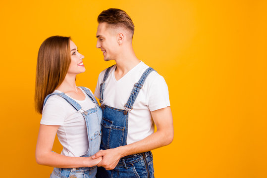 Portrait of cheerful lovely cute couple hugging and holding hands, looking at each other over yellow background, isolated, copy space