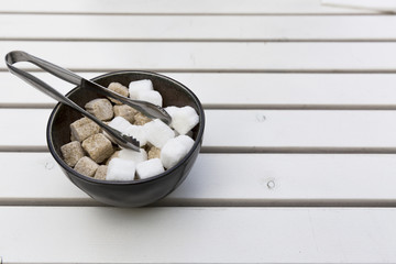 Brown and white sugar cubes in a bowl on a wooden table at cafe